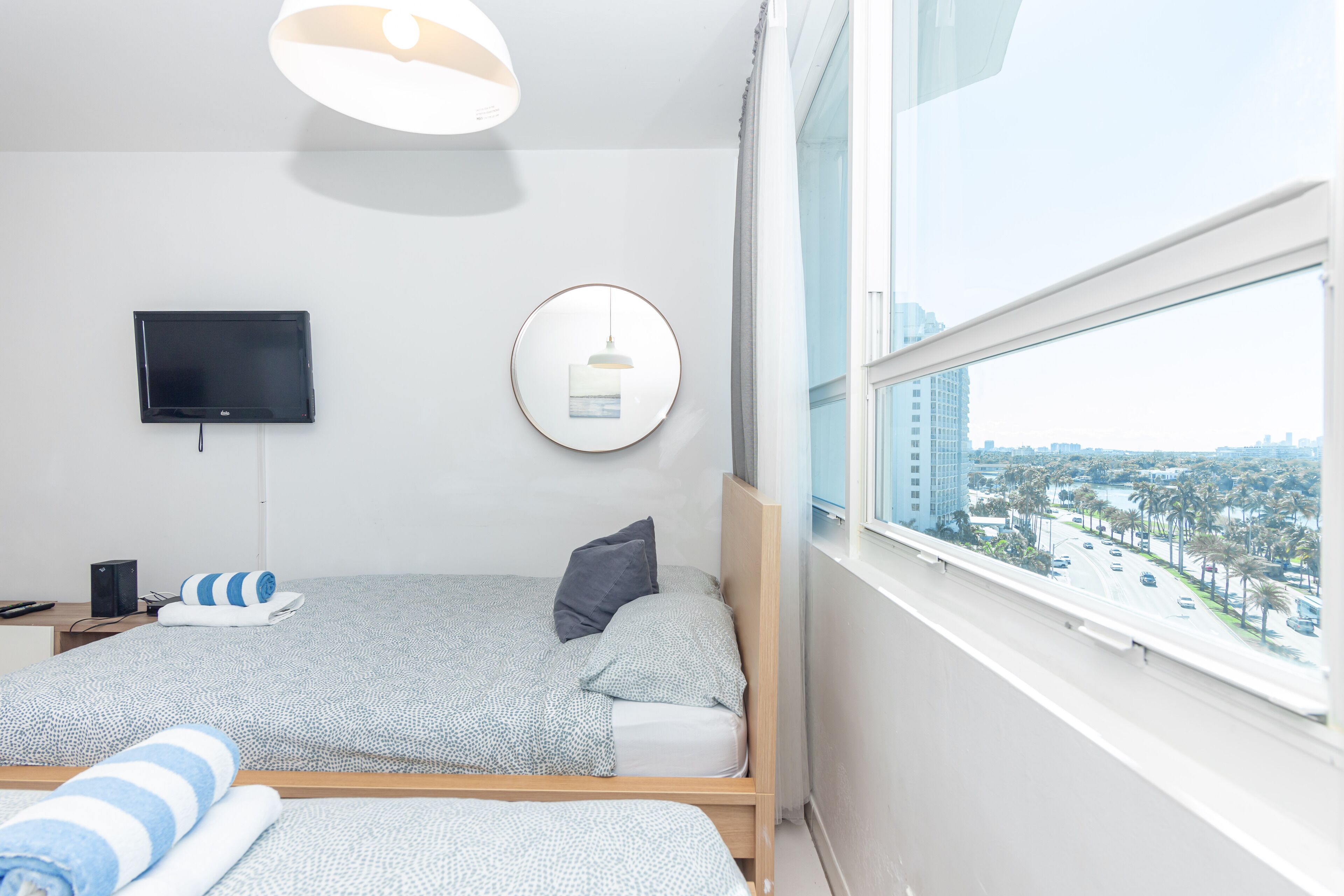 Une chambre avec un lit, une télévision, un miroir rond et une fenêtre donnant sur la ville.