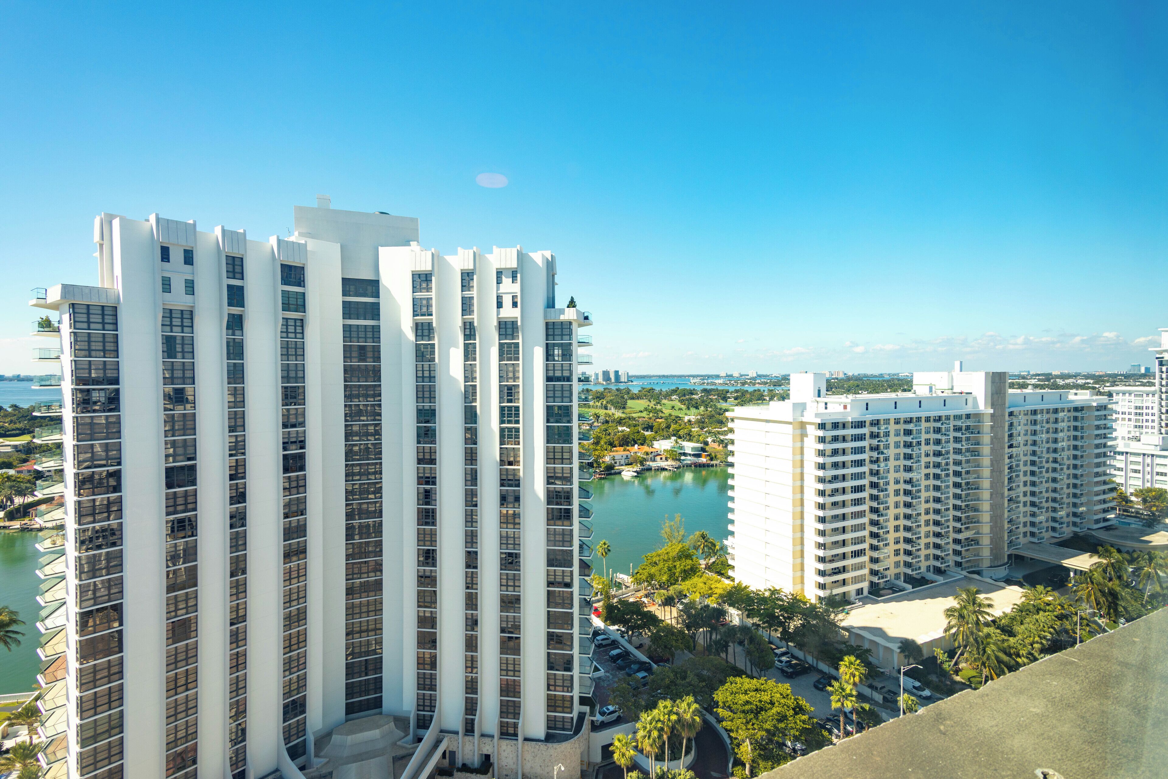 A high-rise hotel with multiple floors, large windows, and a view of a body of water and surrounding greenery.