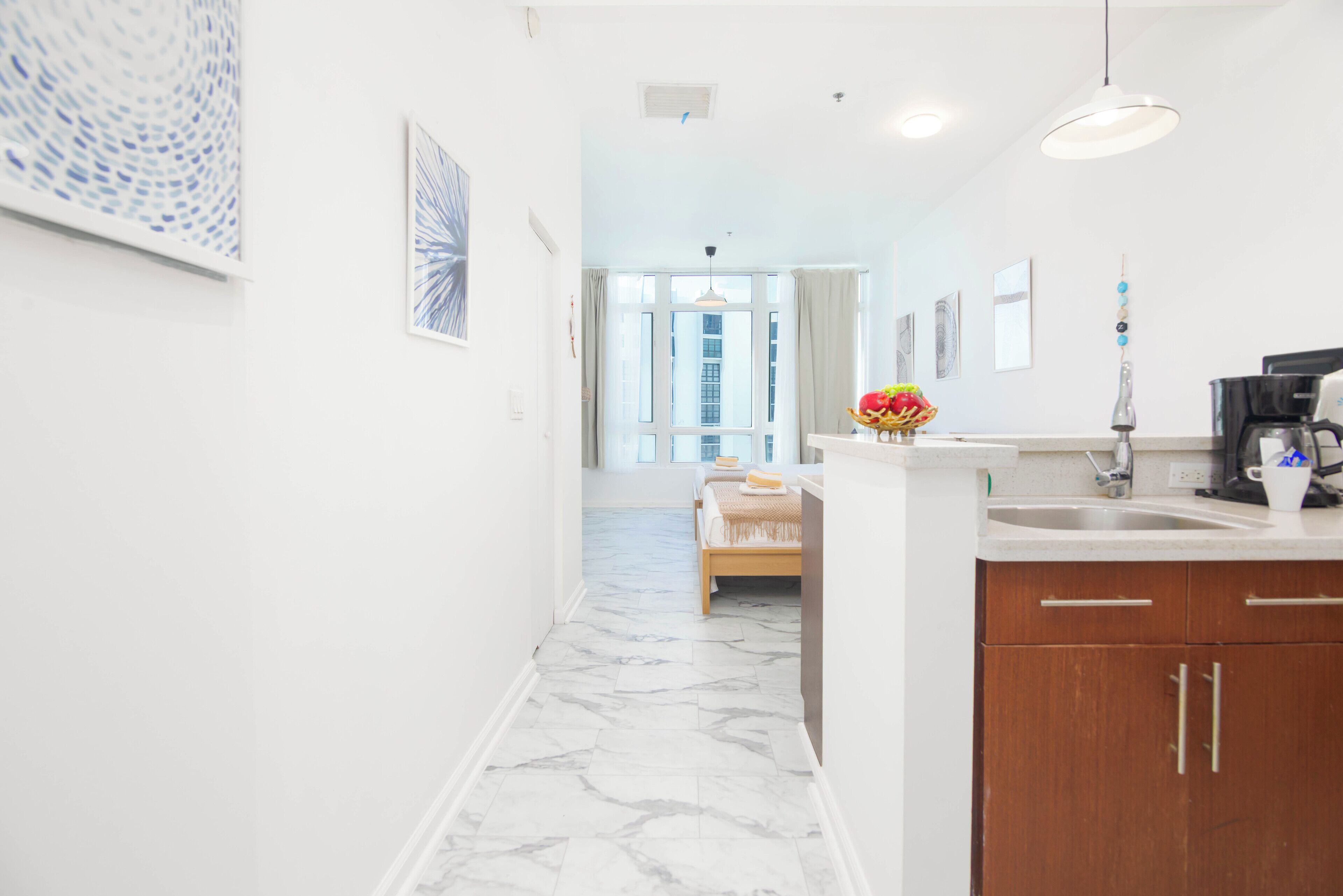 A modern kitchen with marble flooring, wooden cabinets, and a view to the outside.