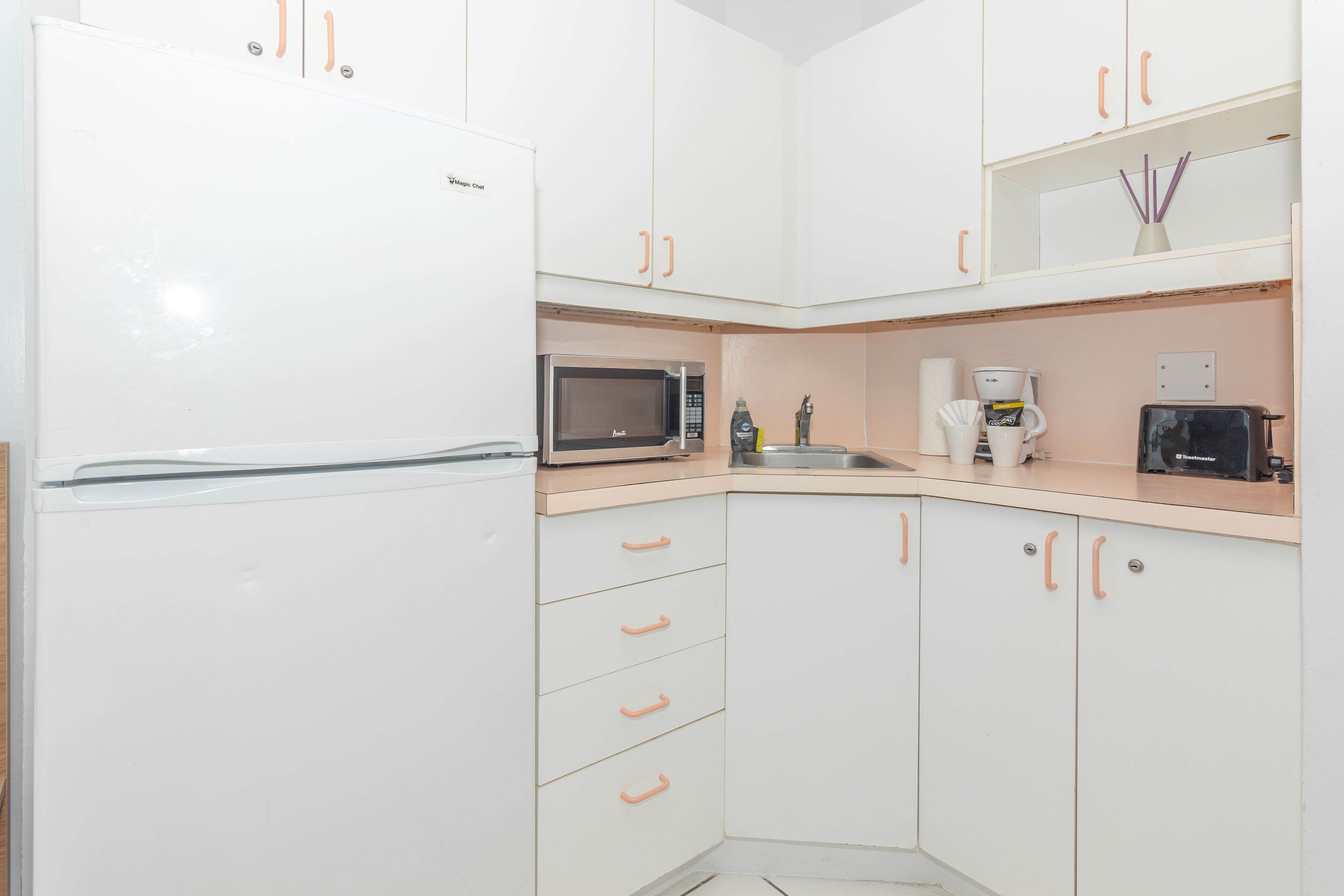 A compact kitchen with white cabinets, a microwave, a toaster, and a coffee maker.