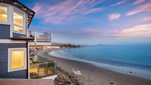 A beachfront property with a balcony overlooking the sea, a clear sky, and a calm beach.