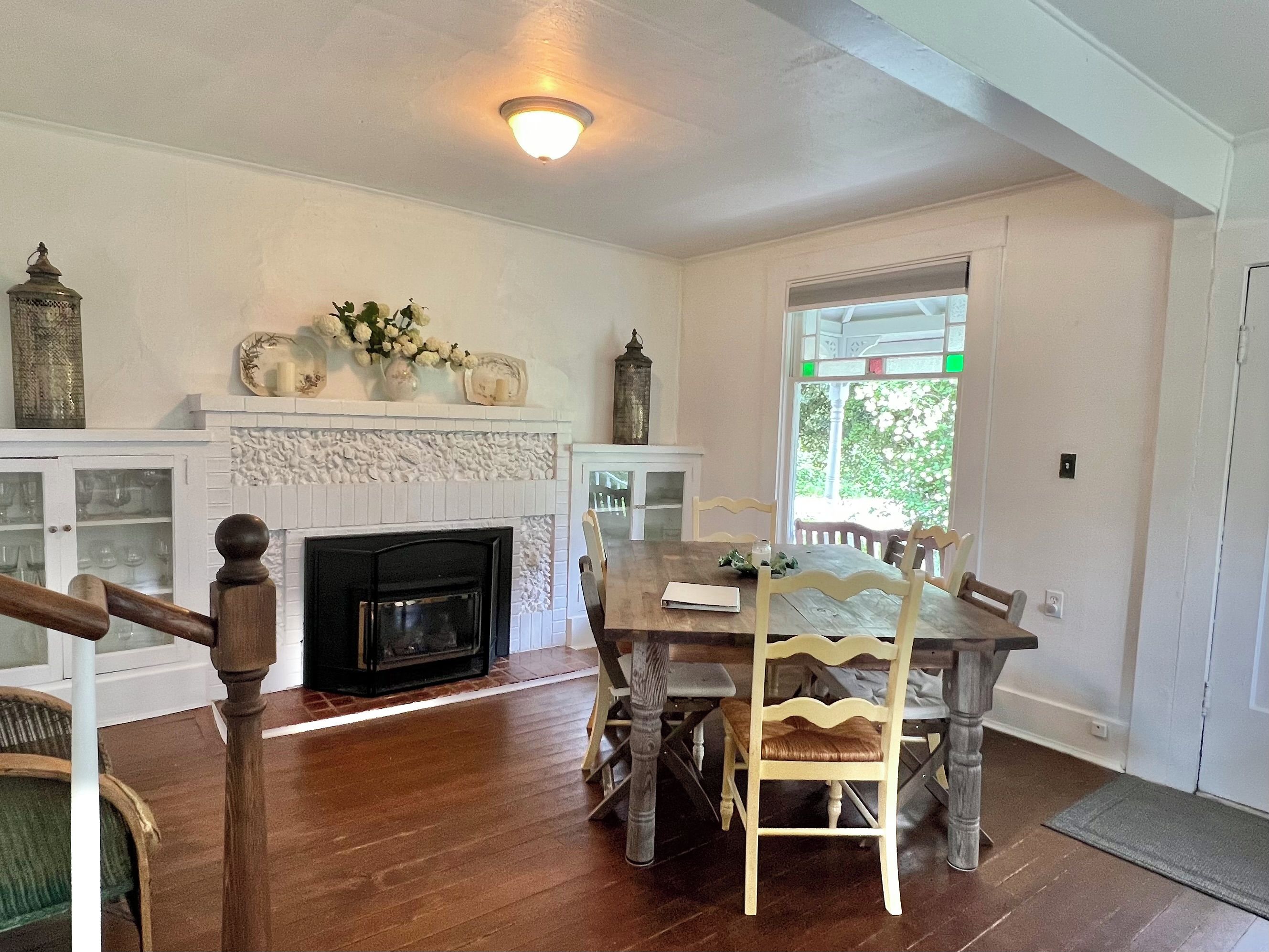 A dining area with a wooden table and chairs, a fireplace, and a view through a window.