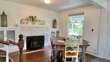 A dining area with a wooden table and chairs, a fireplace, and a view through a window.