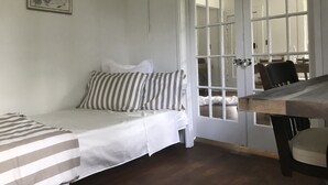 A room with a bed, a chair, and a table. There is a door with glass panels and a framed picture on the wall. - Vashon Farmhouse  (Vashon)