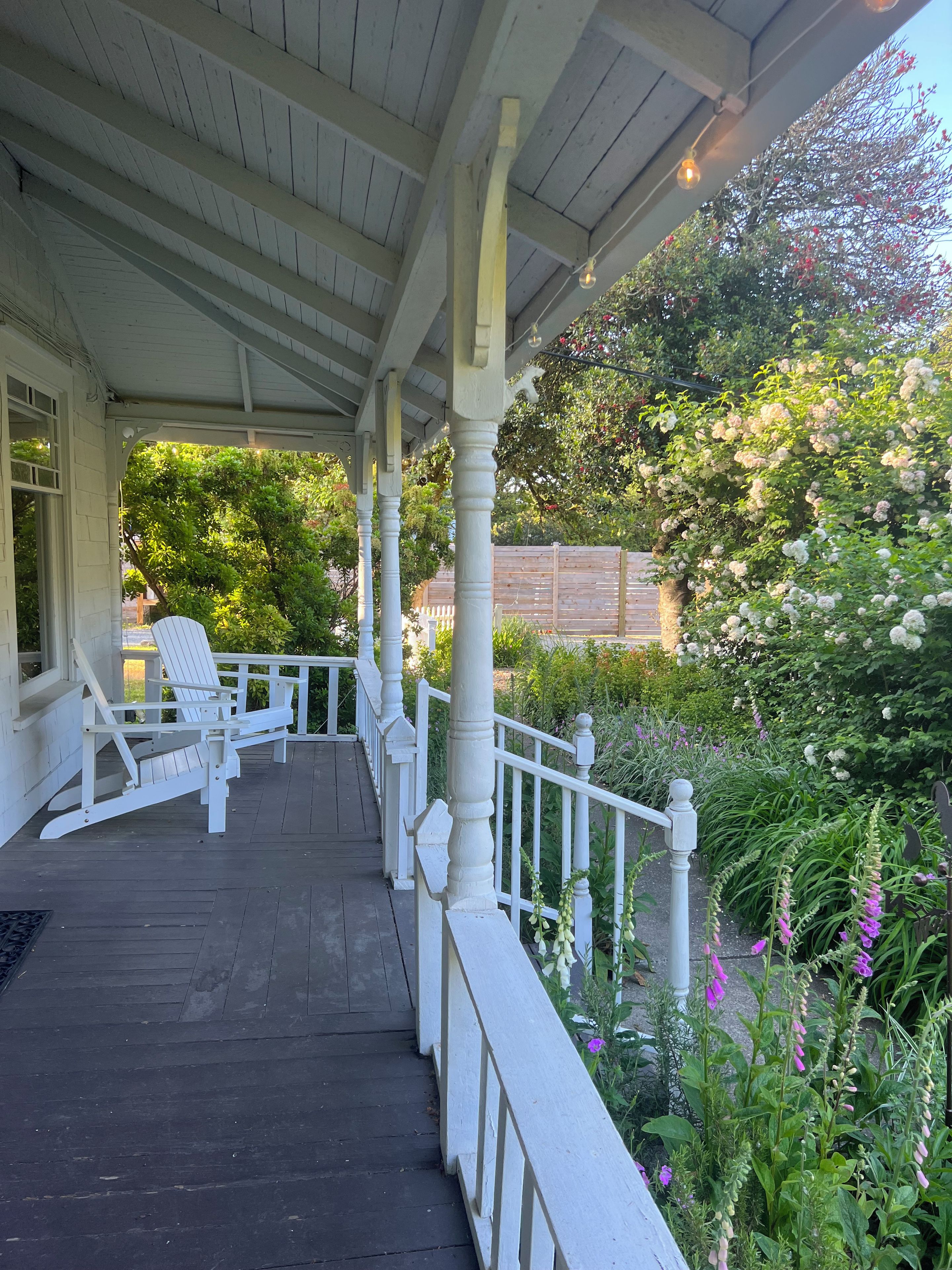 A covered porch with white railings and a row of white Adirondack chairs.