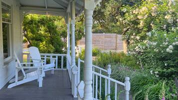 A covered porch with white railings and a row of white Adirondack chairs.