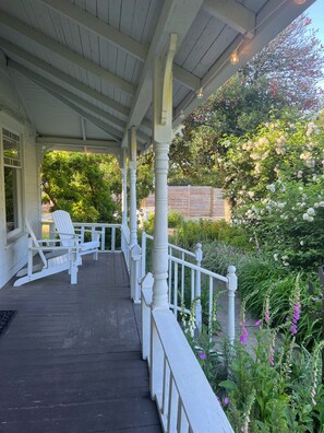 Une véranda couverte avec des balustrades blanches et une rangée de fauteuils Adirondack blancs.