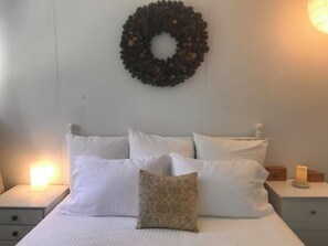 A bed with white bedding, a decorative pillow, a wall-mounted wreath, and bedside tables with candles. - Vashon Farmhouse  (Vashon)