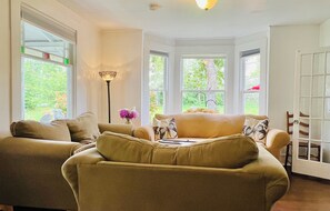 Une pièce chaleureuse avec deux canapés, une lampe sur pied et une vue sur la verdure grâce à de grandes fenêtres.