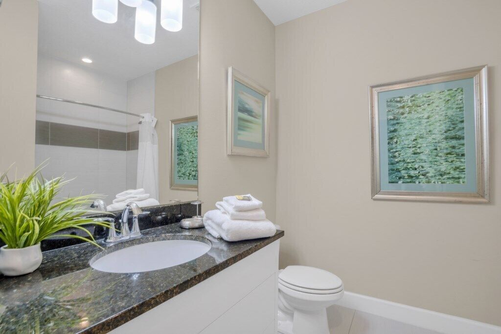 A modern bathroom with a granite countertop sink, a white toilet, and a shower area.