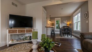 A living room with a flat-screen TV, a dining area with a table and chairs, and a large window.
