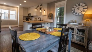 A dining area with a wooden table, chairs, yellow placemats, and a clock on the wall.