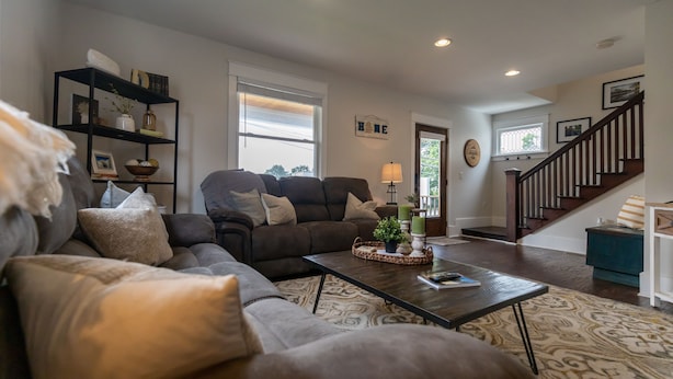 A living room with a sectional sofa, a coffee table, a bookshelf, and a staircase.