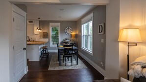 A modern kitchen with a dining area, a clock on the wall, and a lamp by the window.