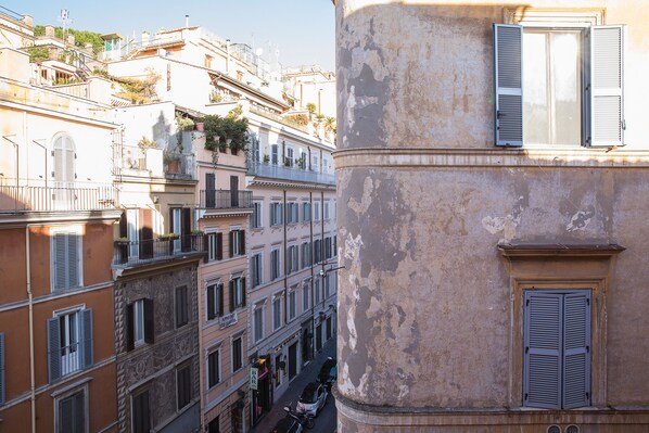 A narrow street between buildings with balconies and shutters, suggesting a historic urban setting. - MAISON Spanish steps (Roma)