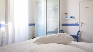 Quarto com cama, guarda-roupa, cadeira e prateleira com artigos de higiene pessoal.