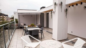 Eine Dachterrasse mit Essbereich, weißen Stühlen und einem runden Tisch mit Feuerstelle.