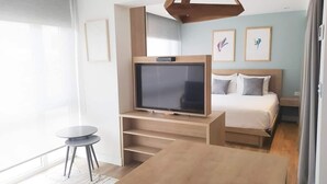 Ein modernes Hotelzimmer mit Fernseher auf einem Holzboden, einem Bett mit weißer Bettwäsche und einem kleinen runden Tisch.