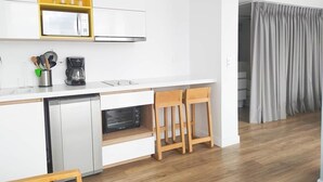 Eine moderne Küche mit weißen Schränken, einem gelben Regal, einer Mikrowelle und einer Kaffeemaschine. Zwei Holzhocker und ein Geschirrspüler sind vorhanden.