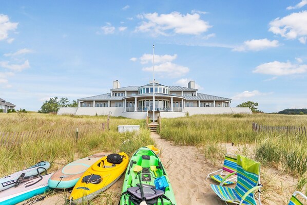 A beach house with a pathway leading to the entrance, kayaks, and beach chairs. - Lake Michigan beach home. Saugatuck. Heated pool, hot tub, 8 bedrooms. 9 baths.  (Saugatuck)