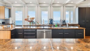 Una cocina moderna con encimeras de granito, electrodomésticos de acero inoxidable y grandes ventanales con vistas al océano.