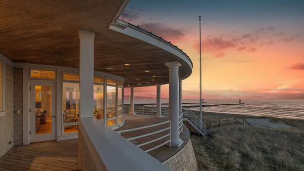Un edificio costero con terraza de madera, columnas blancas y vista al océano al atardecer.