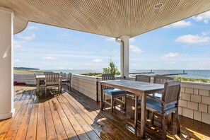A wooden deck with a table and chairs, overlooking a body of water. - Lake Michigan beach home. Saugatuck. Heated pool, hot tub, 8 bedrooms. 9 baths.  (Saugatuck)