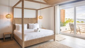A four-poster bed with white linens, a wooden ceiling, and a balcony with a view of the sea.