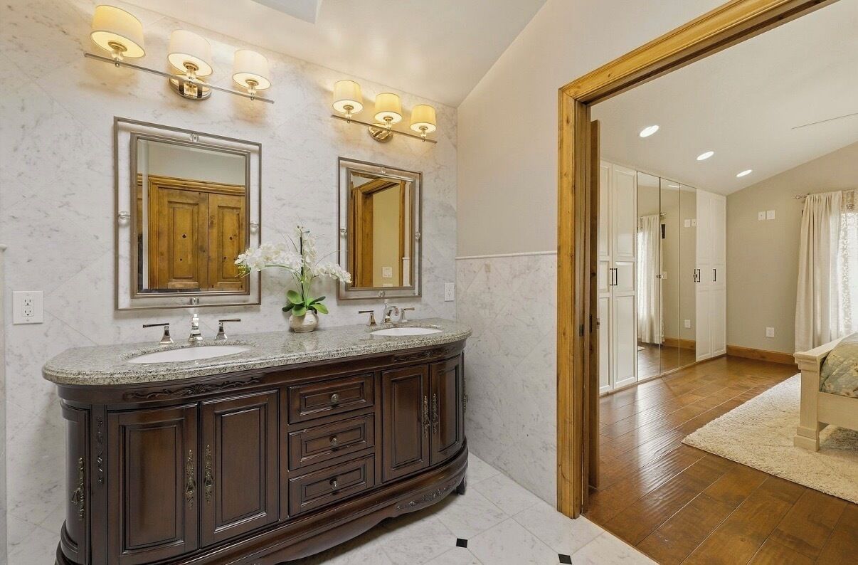 A bathroom with a double vanity, two mirrors, and wall-mounted lighting.