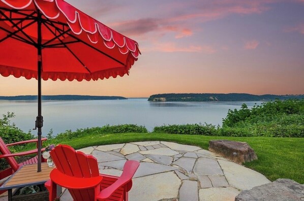 A patio with stone flooring, red Adirondack chairs, and a red umbrella.