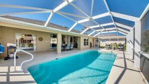 A covered swimming pool with a glass ceiling, a dining area with outdoor seating, and a view of the surrounding landscape. - 2621 SW 27th St. Cape Coral (Cape Coral)