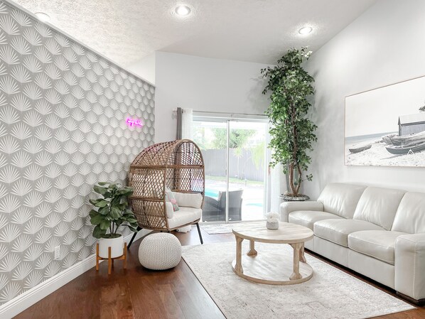 A modern living room with a white sofa, a wicker chair, a round coffee table, and a potted plant.