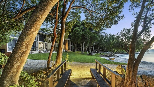 A wooden pathway leading to a building with a glass facade, surrounded by trees and a grassy area. - Waterfront paradise in Key Largo with resort style amenities (Key Largo)