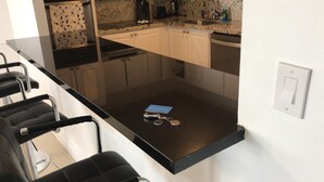 Une cuisine moderne avec une table à manger en verre, des chaises noires et une machine à café.