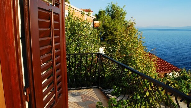 Une porte en bois avec des lattes horizontales, un balcon dallé de pierres et une vue sur la mer.