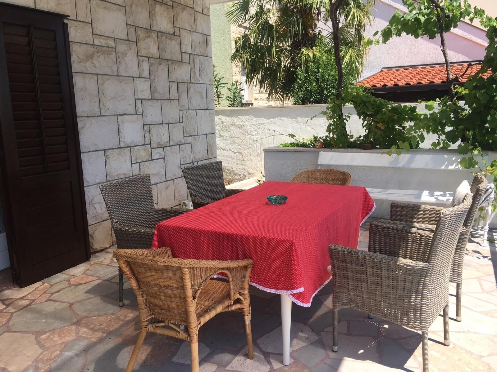 Un patio al aire libre con una mesa cubierta con un mantel rojo, rodeado de sillas de mimbre.