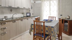 Una cocina con alacenas de madera clara, un lavamanos, un microondas y una mesa de comedor con sillas.