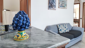 Una sala de estar con una mesa de centro de mármol, un jarrón decorativo azul, un sofá gris con un cojín estampado y dos obras de arte enmarcadas en la pared.