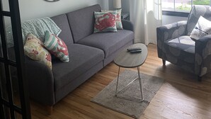 A modern living room with a grey sofa, patterned cushions, a coffee table, and a ceiling fan. - Fern Cottage Crystal Beach (Fort Erie)