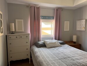 Une chambre à coucher comprenant un lit, une commode, une fenêtre avec des rideaux et des éléments de décoration murale.