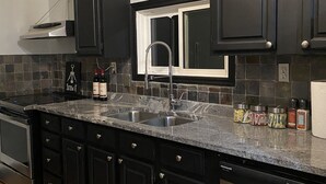 A modern kitchen with dark cabinetry, a stainless steel sink, and a built-in dishwasher. - Fern Cottage Crystal Beach (Fort Erie)