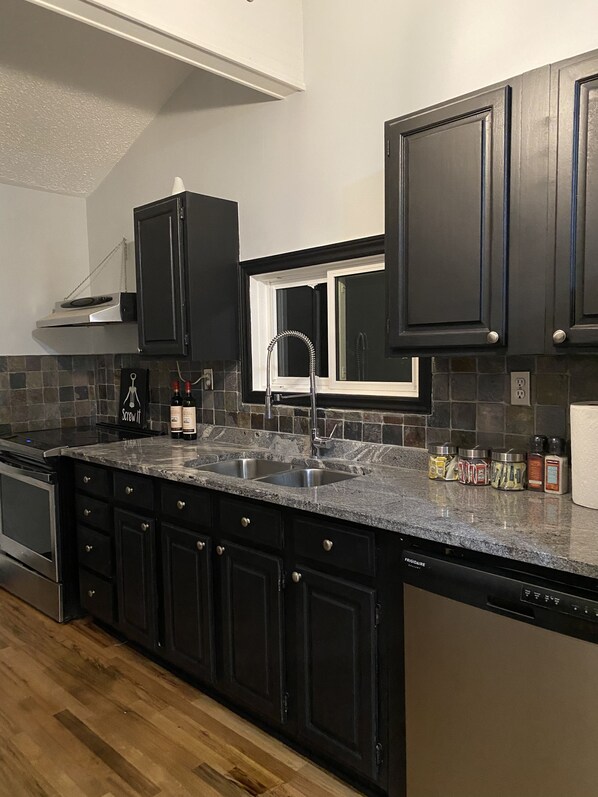 A modern kitchen with dark cabinetry, a stainless steel sink, and a built-in dishwasher. - Fern Cottage Crystal Beach (Fort Erie)