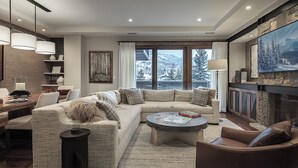 Un salon moderne avec un canapé d’angle, une cheminée et une grande fenêtre donnant sur un paysage enneigé.