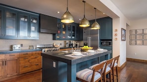 A modern kitchen with dark blue cabinets, a central island, pendant lighting, and a microwave.