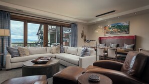 A modern living room with a large sectional sofa, leather armchairs, a coffee table, and a dining area with a high-backed chair.