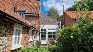 A traditional stone and brick house with a tiled roof, a white-framed window, and a wooden bench in the garden.