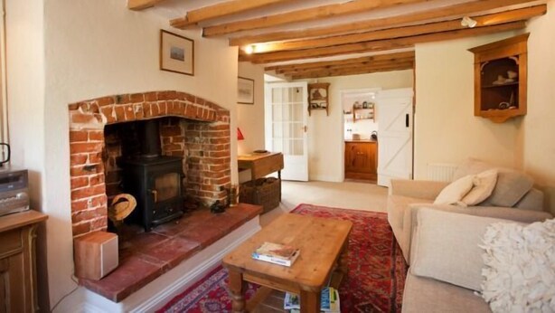 A cozy living room with a brick fireplace, wooden beams, a sofa, and a coffee table.