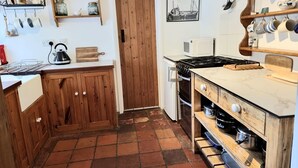 A kitchen with wooden cabinets, a stove, a microwave, and various kitchen utensils on shelves.