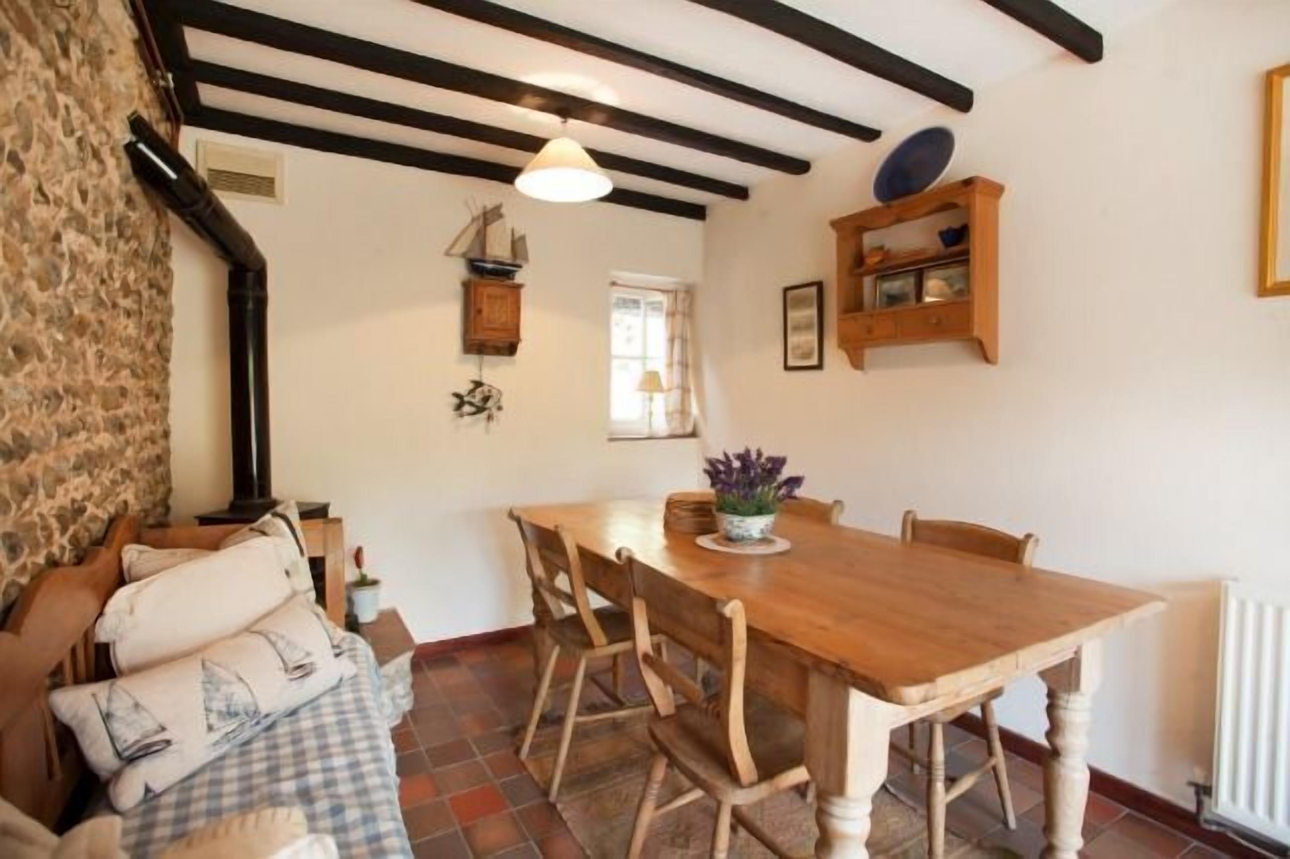Un coin repas avec une table et des chaises en bois, un mur en pierre et une fenêtre avec des rideaux.