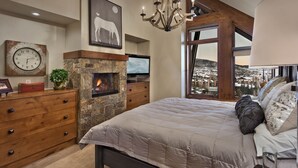 Un dormitorio con chimenea de piedra, una cama grande, un tocador, un reloj y vistas a un paisaje nevado.